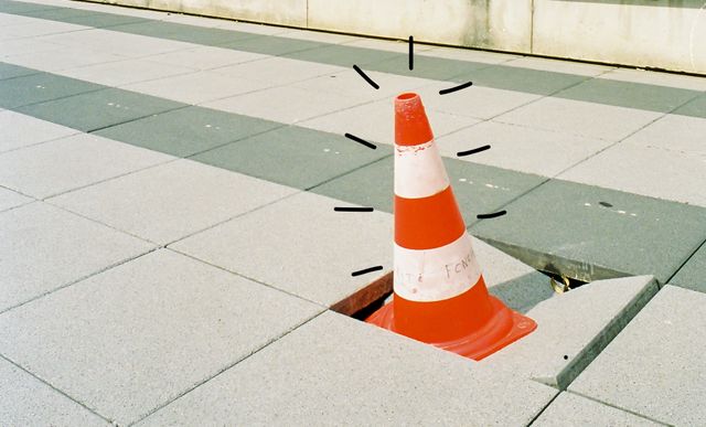 a hole in the sidewalk filed with a caution cone